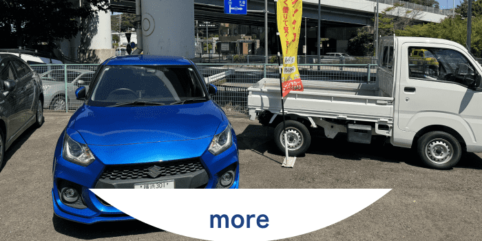 鮮やかな青い乗用車と白い軽トラックが並んで駐車されている中古車販売店の風景