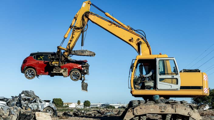 黄色い重機が赤い自動車を吊り上げているスクラップ場の光景