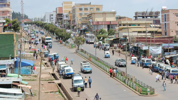 建物が立ち並ぶ街で、道路沿いに停車した車と歩行者の様子