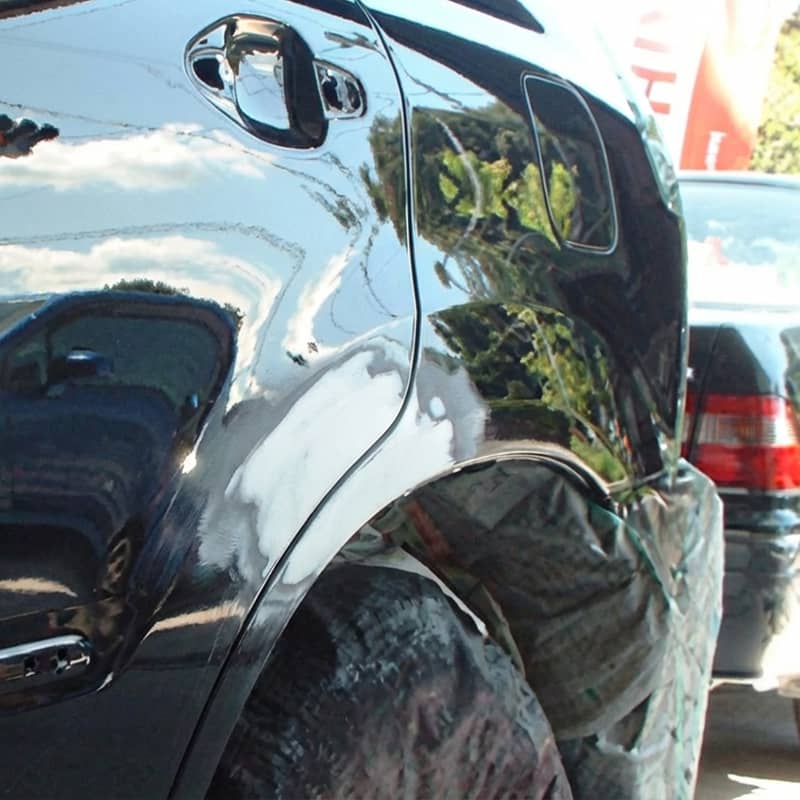 黒い車のリアフェンダーに擦り傷があり、修理のため表面が削られている様子。
