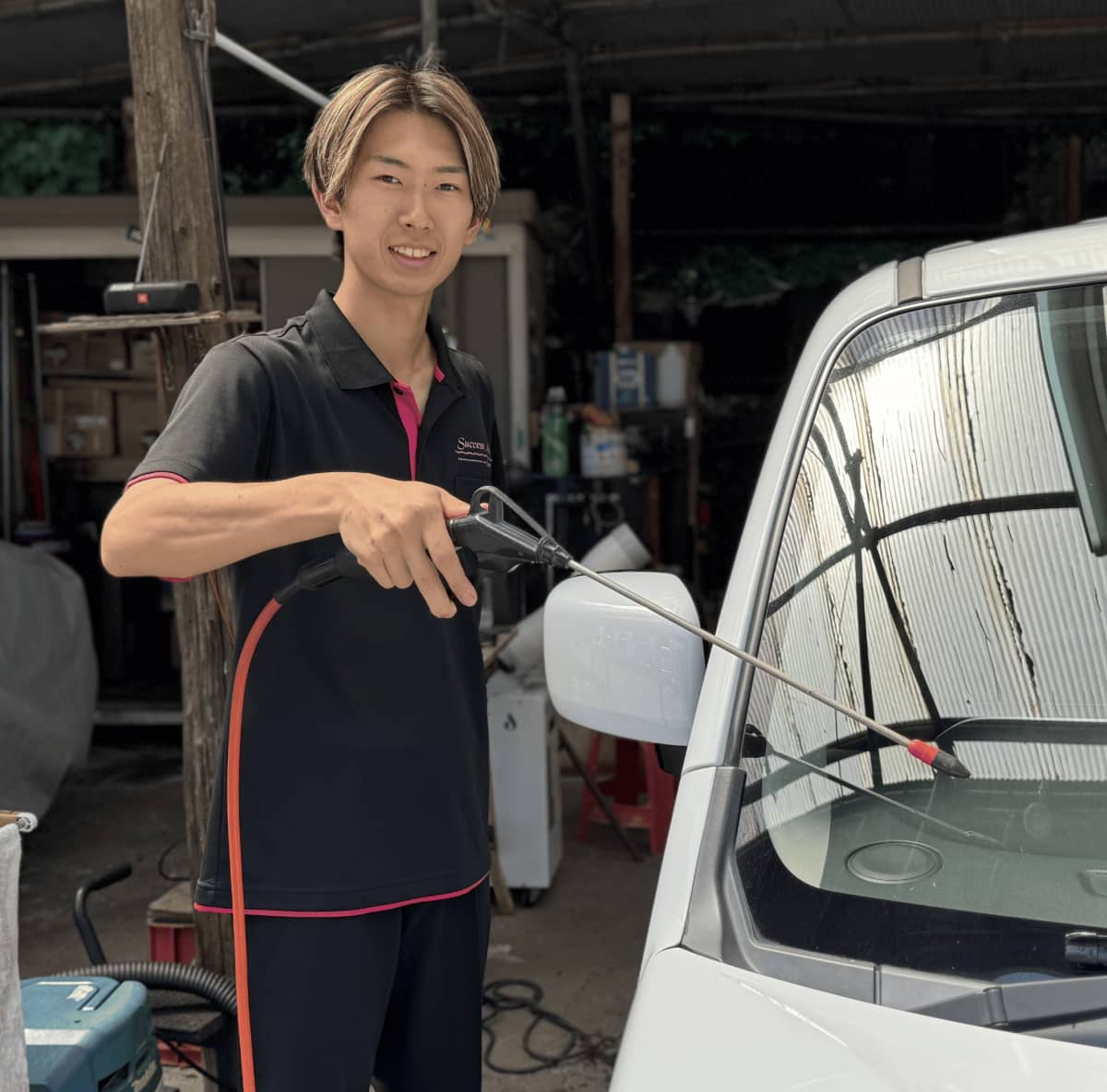 洗車用の高圧洗浄機で白い車のフロントガラスを洗う作業員