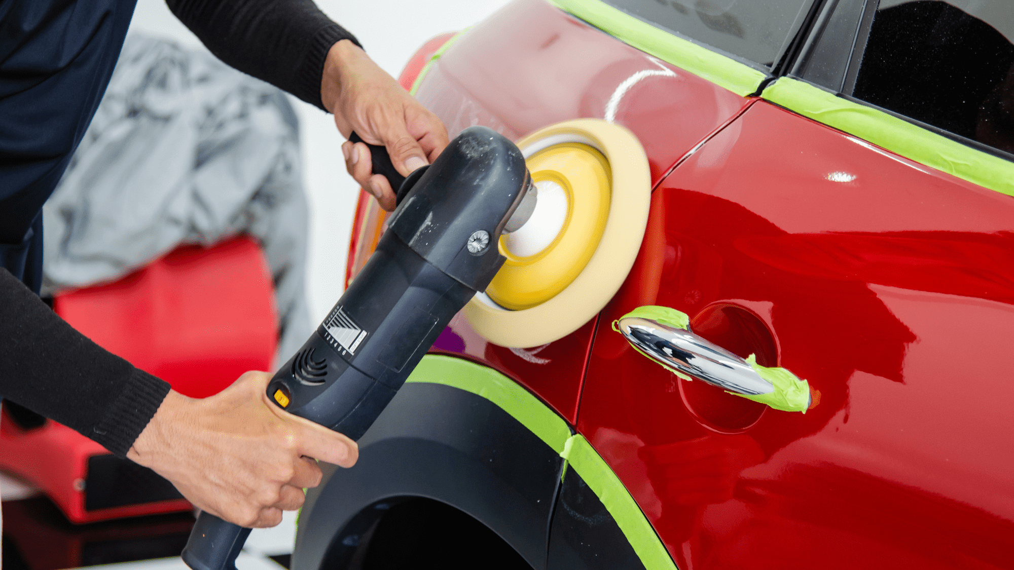 プロのディテイラーが、ポリッシャーを使用して赤い車の塗装面を磨いている様子。傷や汚れを落とし、新車のような輝きを取り戻すための作業です。