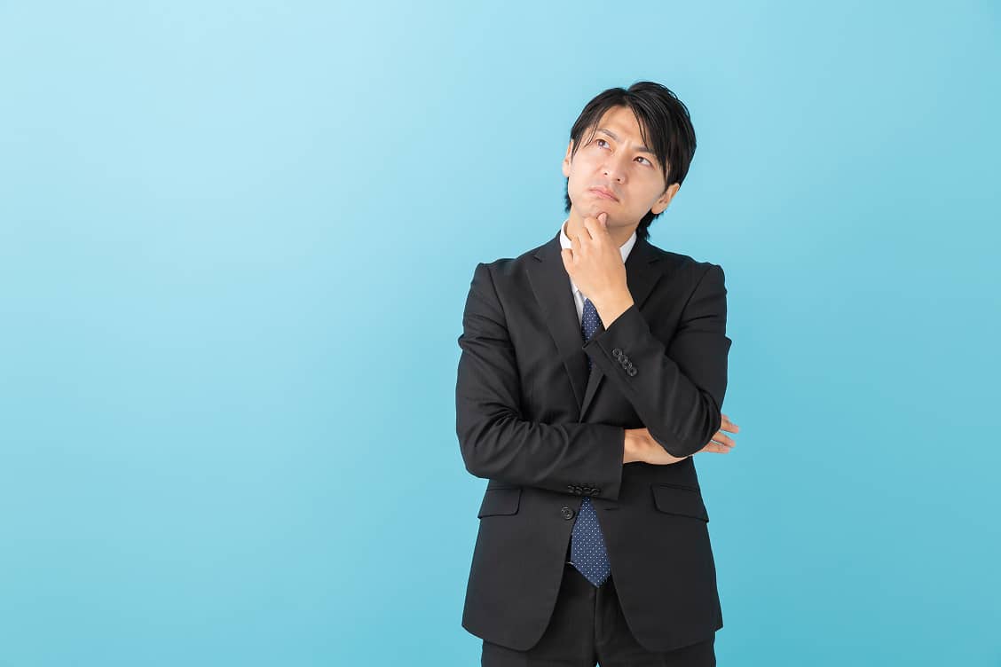 考え込む表情で上を見上げるスーツ姿の男性